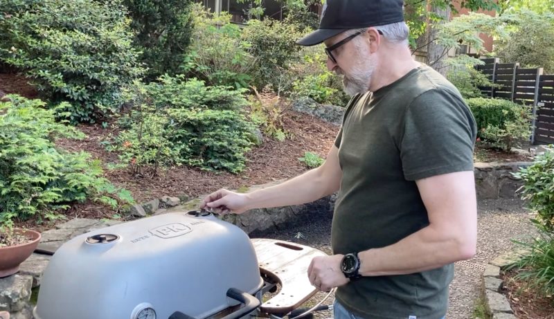 Man adjusting the vent on a PK cast-aluminum charcoal grill outdoors, demonstrating airflow control for temperature precision during grilling.