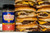Fire & Smoke Society F&S Burger Royale Seasoning Blend 10.2 oz, a container of burger seasoning next to stacked cheeseburgers with beef patties, cheese, pickles, onions, and buns.