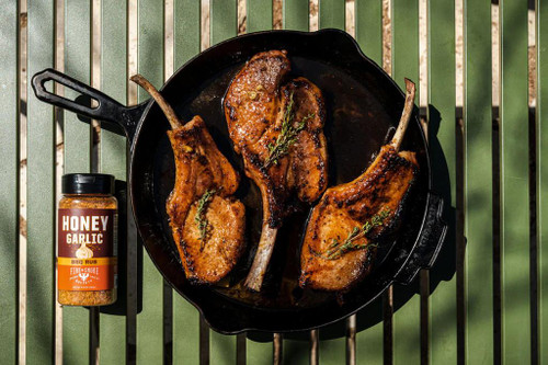 Fire & Smoke Society F&S | HONEY GARLIC BBQ RUB 9.5 OZ, image of grilled lamb chops seasoned with honey garlic BBQ rub garnished with herbs in a black skillet.