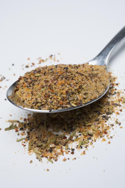 Fire & Smoke Society F&S | The Usual All-Purpose Spice 10.7 oz, ground spice mix with herbs and spices scattered on a white surface with a metal spoon.