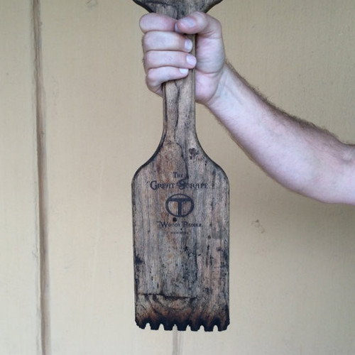 Great Scrape The Great Scrape Woody Paddle Grill Scraper, hands holding a rustic wooden grill scraper paddle with logo engraved, wooden handle and slotted blade design.