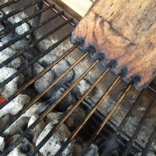 Great Scrape The Great Scrape Woody Paddle Grill Scraper, wooden and metal grill scraper with a scalloped edge resting on a barbecue grill.
