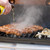 GrillGrate® for The Original & PK300 Grill, cooking sausages and onions on a barbecue grill with steam and grill marks visible.