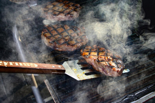 GrillGrate® for The Original & PK300 Grill, a close-up of meat steaks being grilled on the grate with visible grill marks and smoke.