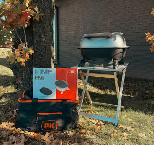 PK Grills Let's PKGO Accessory Bundle, portable cast iron grill with stand, with packaged grill griddle and carrying bag, outdoor setting with fallen leaves and tree trunk