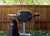 PK Grills PK360 Start Cookin' Bundle - Graphite, outdoor charcoal grill with side tray and cover, set up in a backyard with green trees and wooden fence.