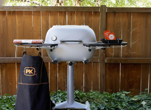 PK Grills PK360 Start Cookin' Bundle - Silver, outdoor kitchen grill with side tray, thermometer, and carrying bag, set against a wooden fence and greenery.