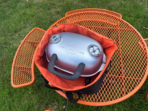 PK Grills PKGO Carrying Bag, portable grill stored inside a black and orange carrying bag on a green grassy surface.