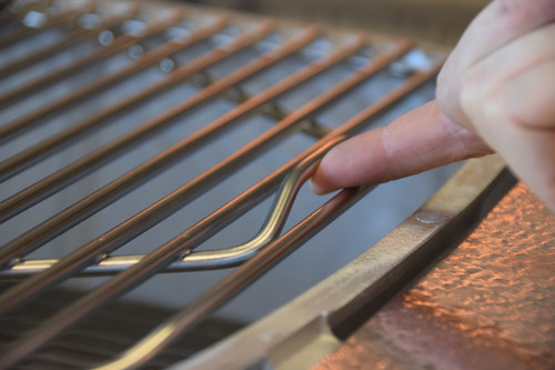 PK Grills Stainless Steel Cooking Grid for Original PK, close-up of a stainless steel cooking grill being cleaned with a wire brush.
