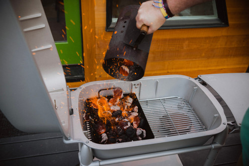 PK Grills The PK Heavy Duty Charcoal Basket, metal charcoal basket being handled over a portable grill with hot sparks flying.