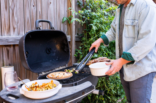 PK Grills The PK360 Grill & Smoker - Classic Silver, outdoor grilling with a person cooking food on a barbecue grill in a backyard setting.