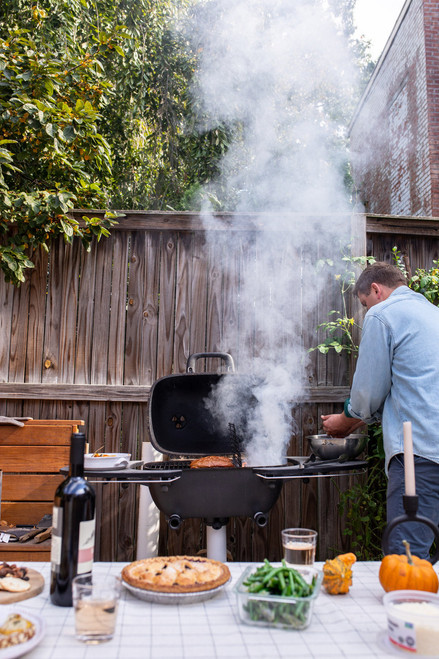 PK Grills The PK360 Grill & Smoker - Classic Silver, outdoor barbecue grill with smoke rising, set in backyard with food and drinks on table.
