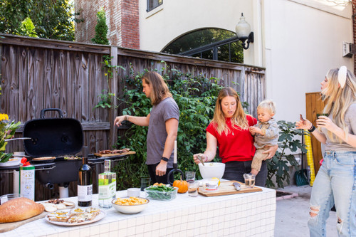 PK Grills The PK360 Grill & Smoker - Classic Silver, outdoor barbecue setup with people grilling and socializing in a backyard.